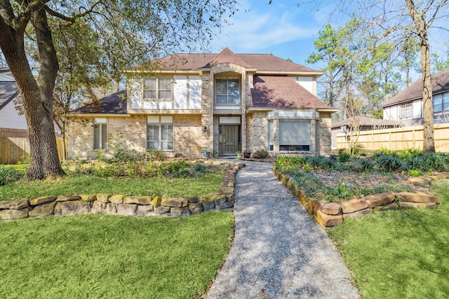 view of front facade with a shingled roof, a front yard, brick siding, and fence