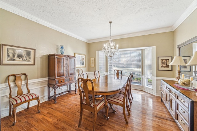 dining area with a wainscoted wall, ornamental molding, a textured ceiling, wood finished floors, and a chandelier