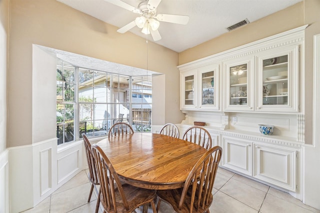 dining space featuring a wainscoted wall, light tile patterned floors, visible vents, a decorative wall, and ceiling fan