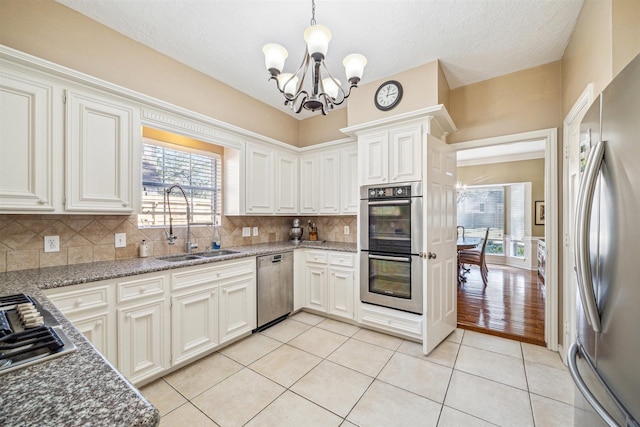 kitchen with backsplash, an inviting chandelier, appliances with stainless steel finishes, light tile patterned flooring, and a sink