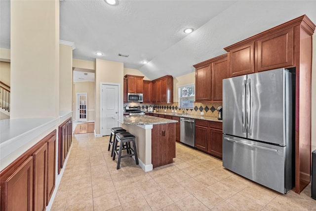 kitchen featuring a center island, a breakfast bar area, stainless steel appliances, lofted ceiling, and backsplash