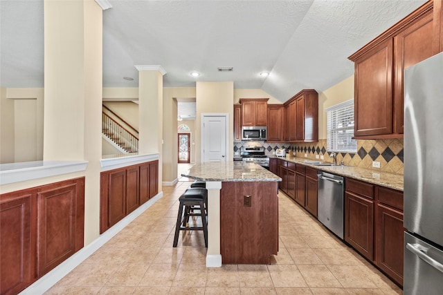 kitchen with light tile patterned flooring, stainless steel appliances, a sink, light stone countertops, and a kitchen bar