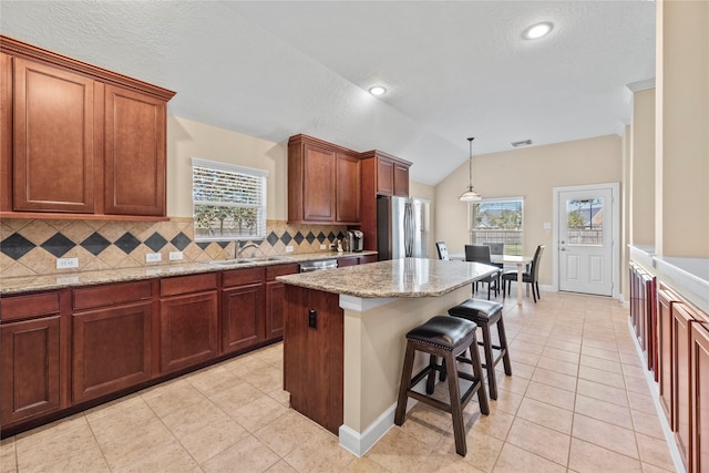 kitchen with lofted ceiling, stainless steel appliances, a sink, a kitchen breakfast bar, and backsplash