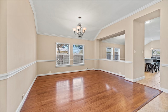 spare room with a wealth of natural light, a chandelier, vaulted ceiling, and wood finished floors