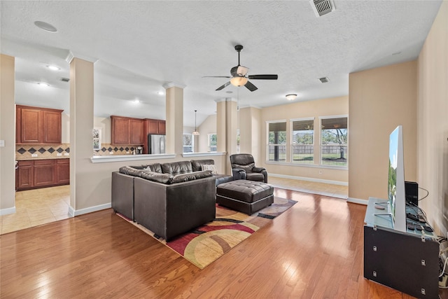 living area with decorative columns, visible vents, baseboards, light wood-style flooring, and a textured ceiling