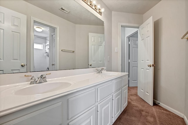 full bathroom with double vanity, a textured ceiling, baseboards, and a sink