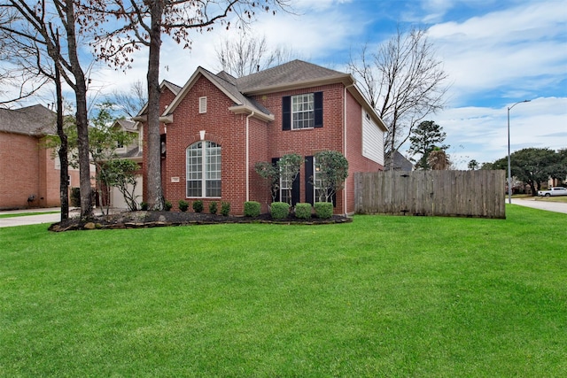 traditional-style house featuring an attached garage, brick siding, fence, and a front lawn