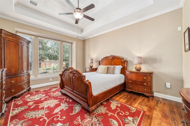 bedroom featuring a tray ceiling, wood finished floors, visible vents, and crown molding