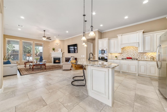 kitchen with appliances with stainless steel finishes, open floor plan, light stone countertops, a lit fireplace, and a sink