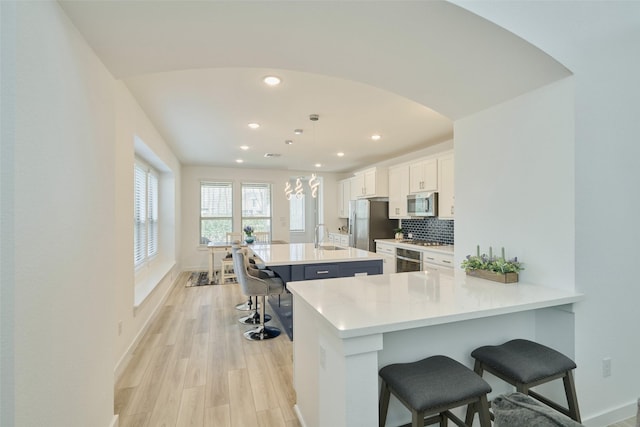 kitchen featuring arched walkways, stainless steel appliances, a sink, tasteful backsplash, and a kitchen bar