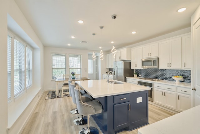 kitchen featuring stainless steel appliances, light wood-style flooring, white cabinetry, and decorative backsplash