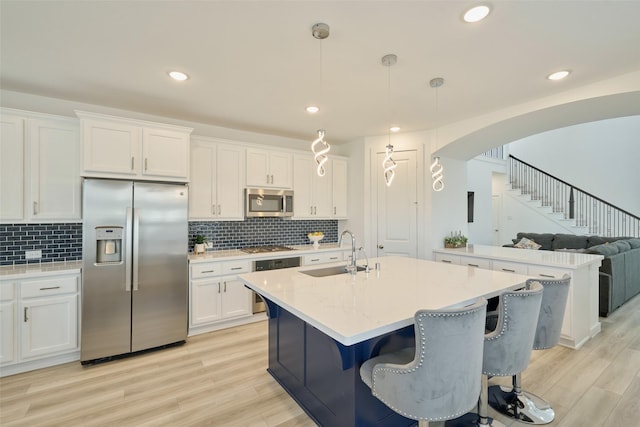 kitchen with arched walkways, light wood-style flooring, appliances with stainless steel finishes, white cabinetry, and a sink