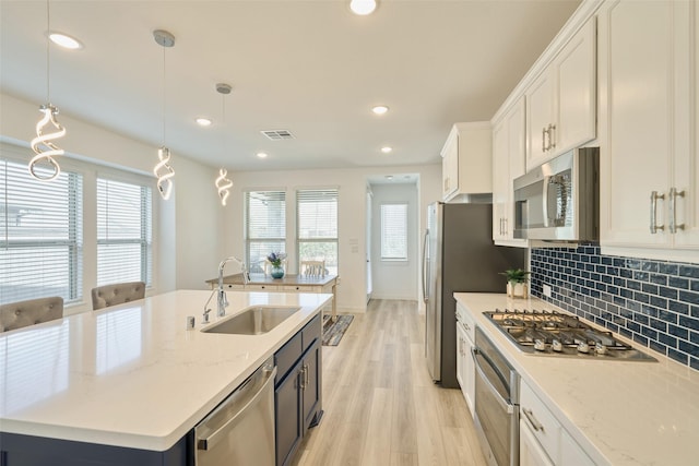 kitchen featuring stainless steel appliances, a sink, white cabinetry, decorative backsplash, and light wood finished floors