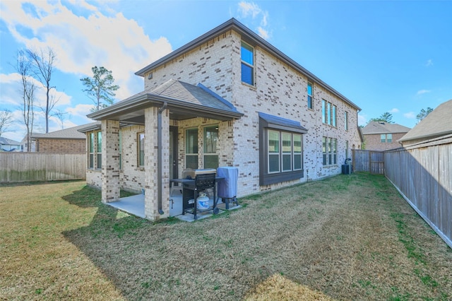 rear view of property featuring a fenced backyard, a lawn, brick siding, and a patio