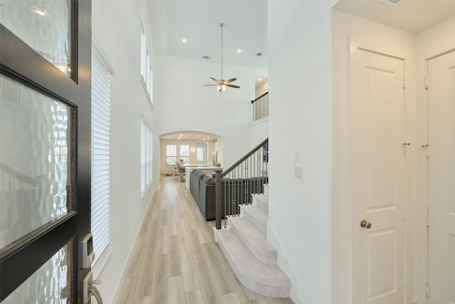 foyer entrance featuring arched walkways, recessed lighting, a towering ceiling, stairway, and light wood-type flooring