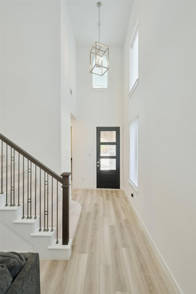 entrance foyer featuring light wood finished floors, baseboards, a high ceiling, stairs, and a notable chandelier