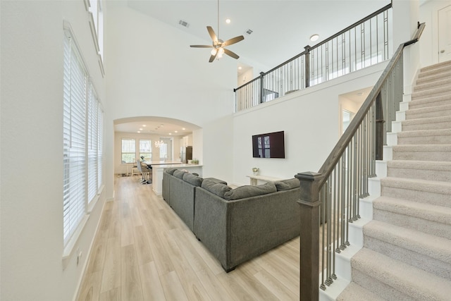 living room featuring arched walkways, ceiling fan, visible vents, stairs, and light wood-type flooring