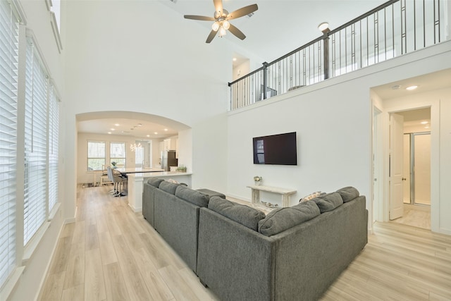 living room with a ceiling fan, arched walkways, light wood-style flooring, and a towering ceiling