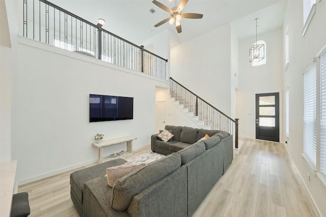 living area with light wood-type flooring, stairs, baseboards, and ceiling fan with notable chandelier