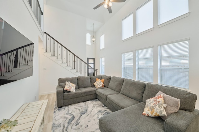 living area with ceiling fan with notable chandelier, stairway, wood finished floors, and baseboards