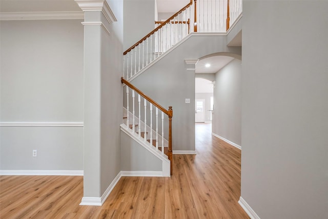 stairs with arched walkways, wood finished floors, a towering ceiling, baseboards, and ornate columns