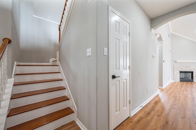 stairway featuring baseboards, arched walkways, wood finished floors, and a stone fireplace