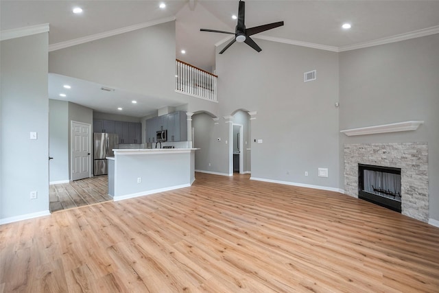 unfurnished living room featuring light wood finished floors, a stone fireplace, visible vents, and crown molding