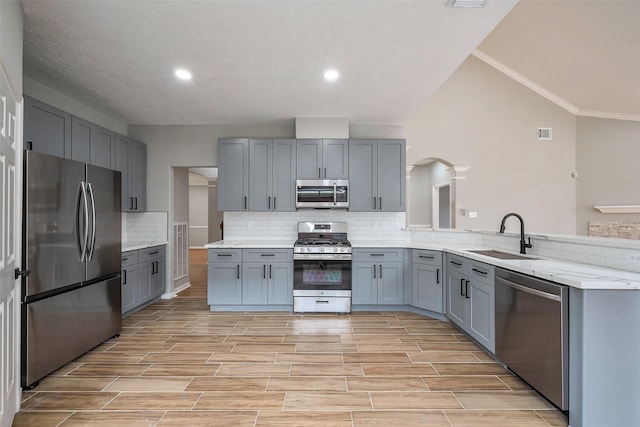 kitchen with a peninsula, gray cabinets, stainless steel appliances, and a sink