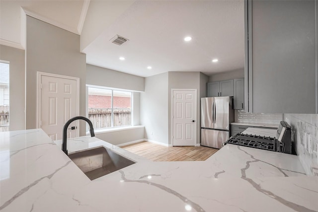 kitchen featuring visible vents, freestanding refrigerator, gas range oven, gray cabinets, and a sink