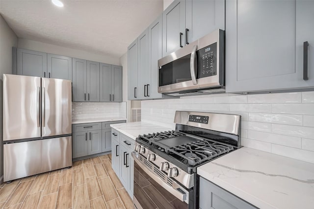 kitchen with light stone counters, wood finish floors, stainless steel appliances, tasteful backsplash, and gray cabinetry