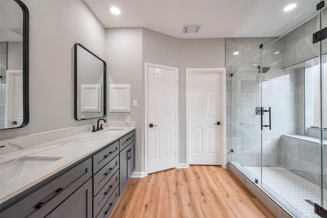 full bath with double vanity, a shower stall, a sink, and wood finished floors