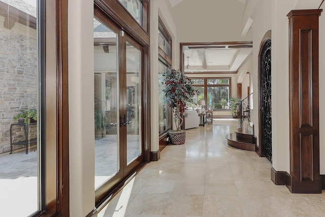 hall with arched walkways, a tray ceiling, french doors, and light tile patterned flooring