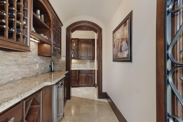 bar with arched walkways, light tile patterned floors, tasteful backsplash, wet bar, and baseboards