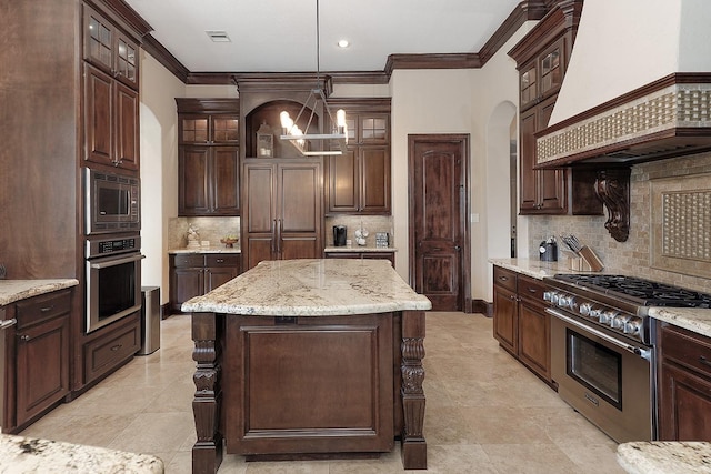 kitchen with arched walkways, built in appliances, custom exhaust hood, dark brown cabinets, and a chandelier