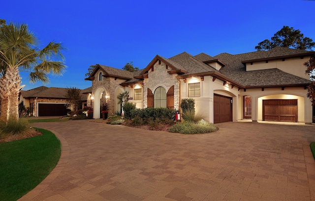 view of front of house featuring a garage, stone siding, decorative driveway, and stucco siding