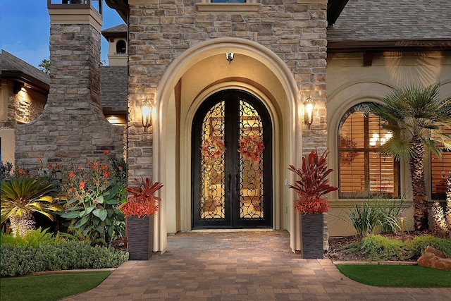 doorway to property with stone siding, roof with shingles, and stucco siding