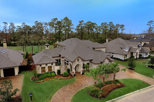 french country inspired facade with stone siding, decorative driveway, and a front yard