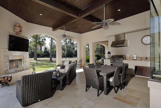 view of patio featuring ceiling fan, a grill, fence, outdoor dining area, and an outdoor stone fireplace