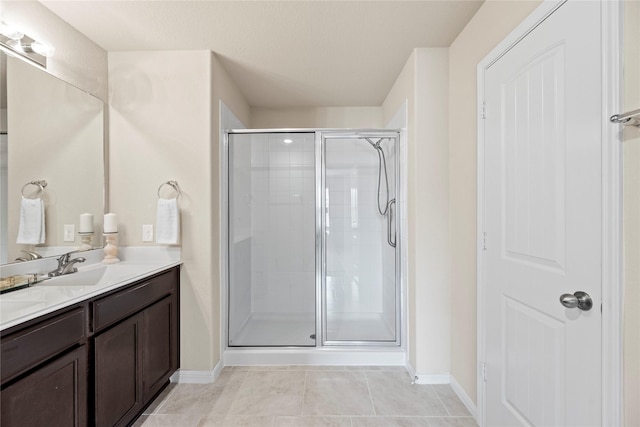 full bath featuring tile patterned flooring, a sink, baseboards, double vanity, and a stall shower