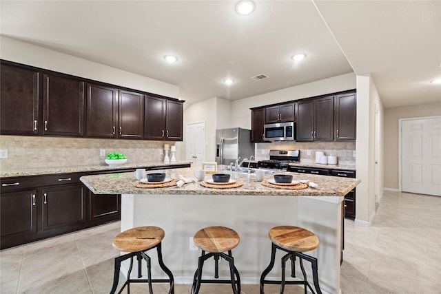 kitchen with stainless steel appliances, visible vents, dark brown cabinets, an island with sink, and a kitchen bar