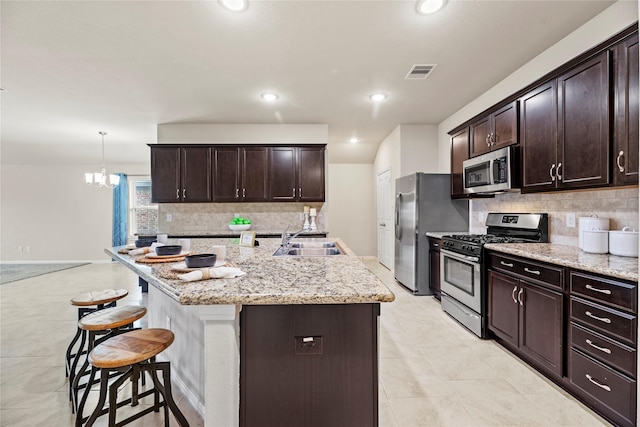 kitchen with light stone counters, dark brown cabinetry, a breakfast bar, a sink, and appliances with stainless steel finishes