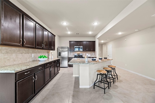 kitchen with baseboards, a kitchen breakfast bar, light stone countertops, stainless steel appliances, and dark brown cabinets