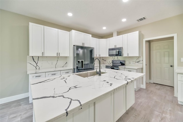 kitchen featuring backsplash, white cabinetry, a sink, light stone countertops, and black appliances