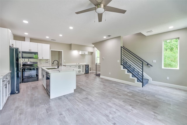 kitchen with recessed lighting, white cabinetry, a sink, an island with sink, and black appliances