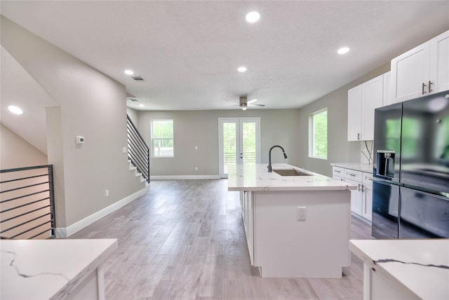 kitchen with a sink, light stone countertops, white cabinetry, and black fridge