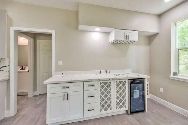 interior space with beverage cooler, a sink, light wood-style floors, baseboards, and a bar