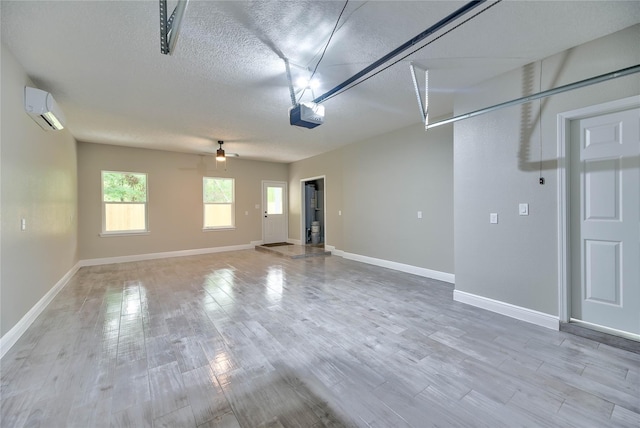 garage featuring ceiling fan, baseboards, an AC wall unit, and a garage door opener