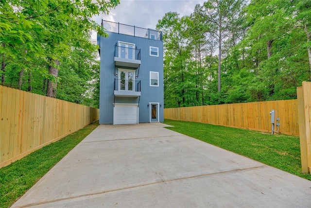 view of front facade with a garage, concrete driveway, a balcony, fence, and a front yard