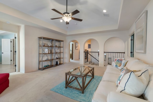 living room with carpet, arched walkways, a tray ceiling, visible vents, and ceiling fan