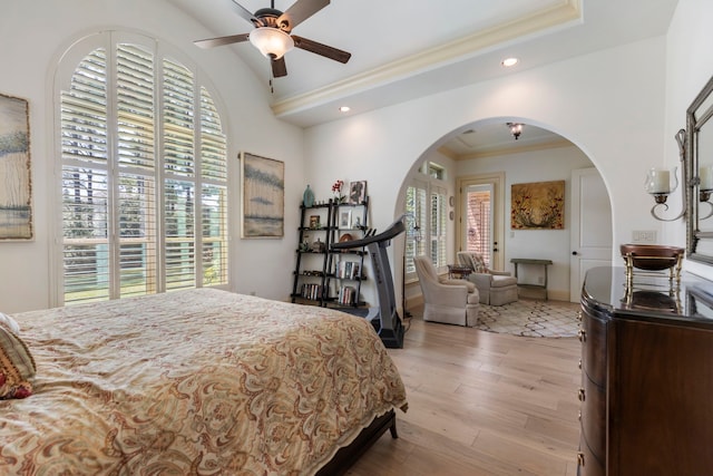 bedroom with ornamental molding, arched walkways, multiple windows, and wood finished floors